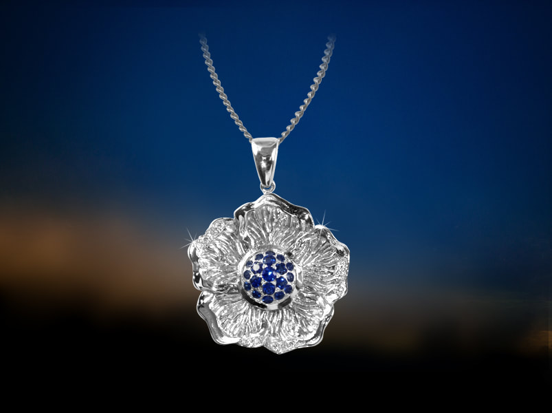 Stylised hibiscus flower pendant in white gold and sapphire centre